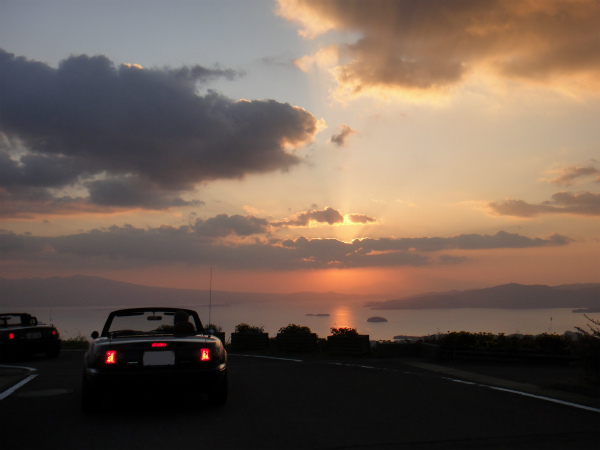 朝日が昇り美しく照らし出される海と島とロードスター